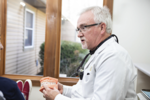Dr. Kinney sits in the office and holds a model set of teeth